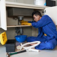 asian-plumber-blue-overalls-clearing-blockage-drain